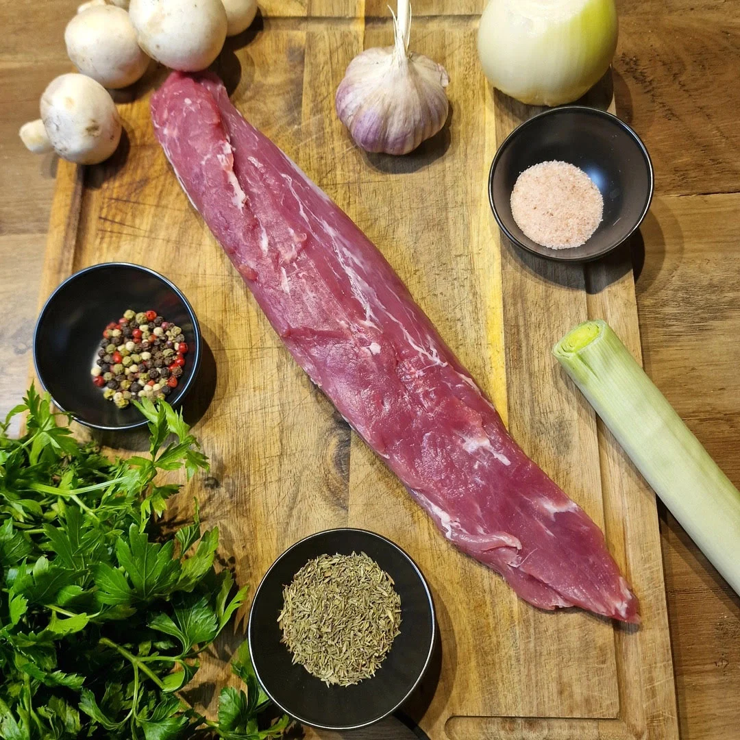 Składniki do polędwiczki faszerowanej: polędwiczka wieprzowa, pieczarki, por, ser żółty, czosnek i przyprawy ułożone na drewnianej desce.