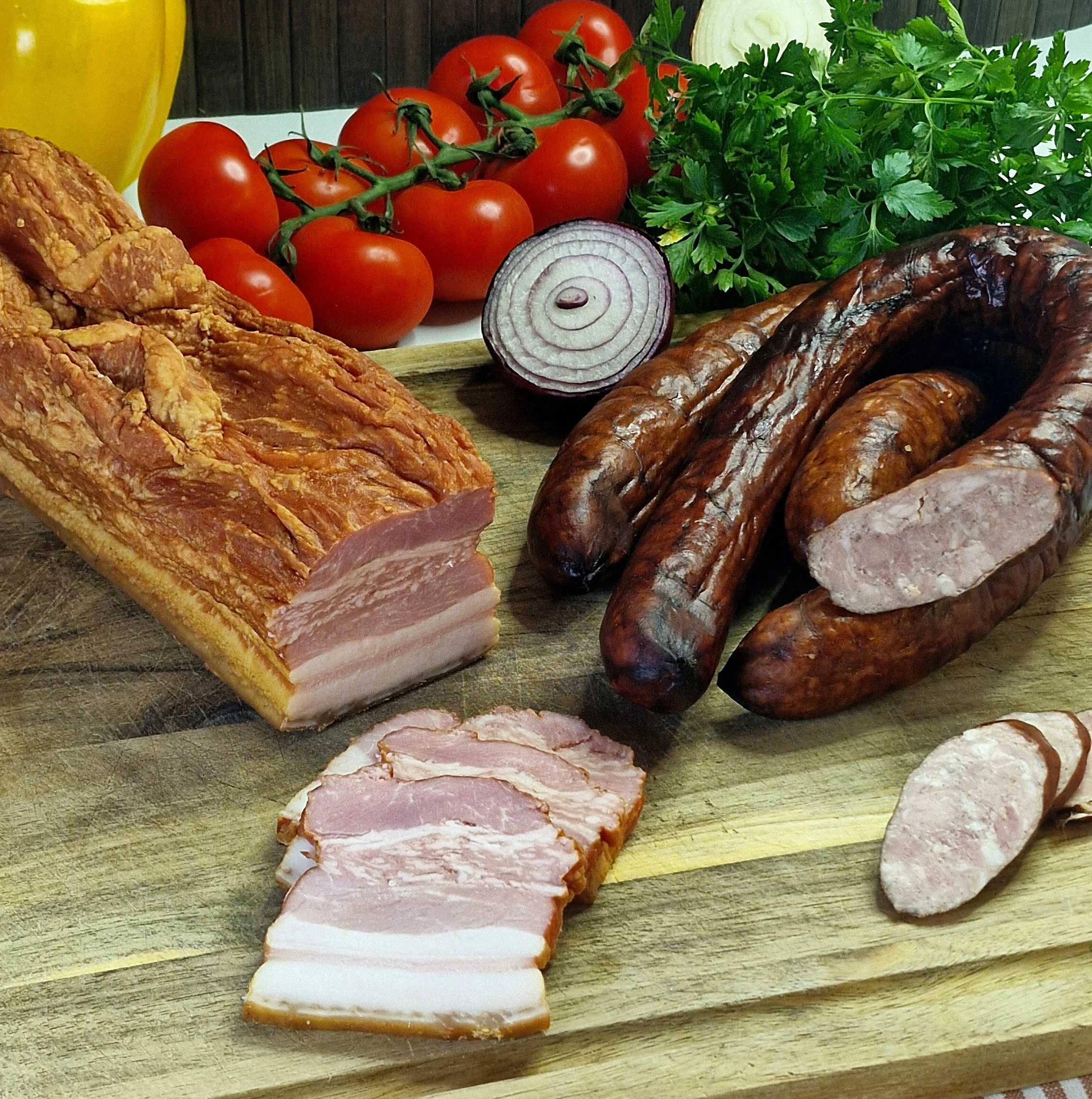 Składniki na deskach: kiełbasa swoja, boczek, warzywa i przyprawy do mięsnej patelni